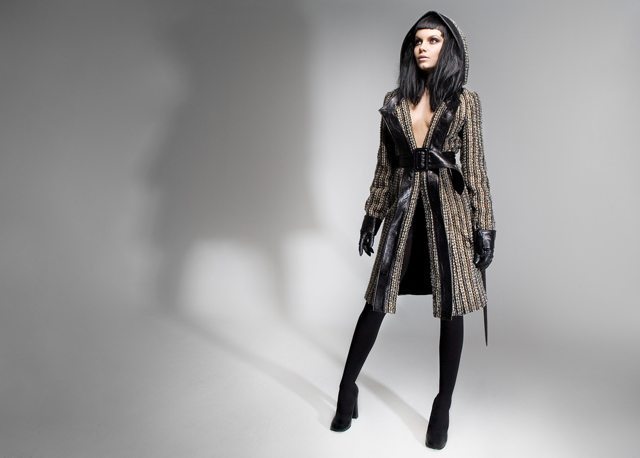 Modelo con un abrigo de lana con capucha, cinturón ancho, guantes y botas altas sobre fondo gris claro.